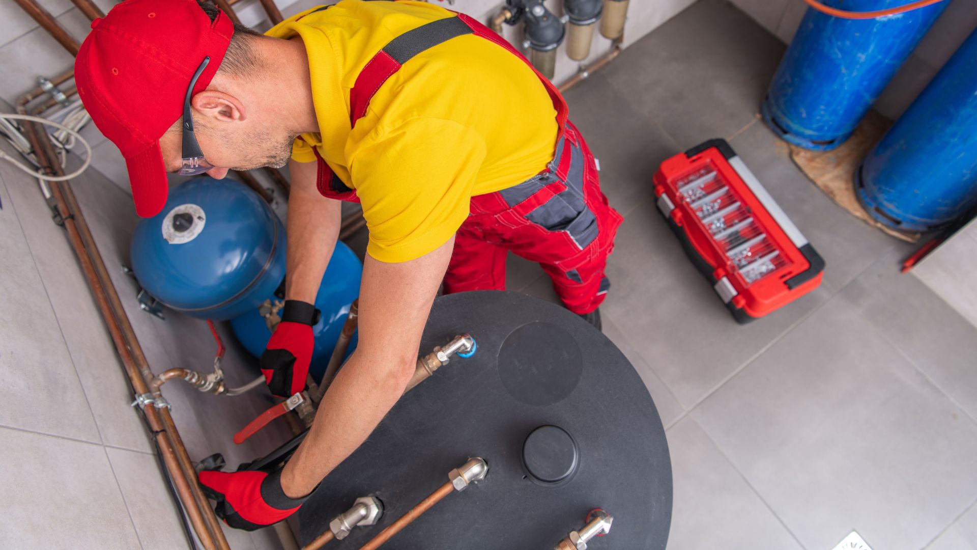 Plumber working on top of a floor-standing water heater, seen from above